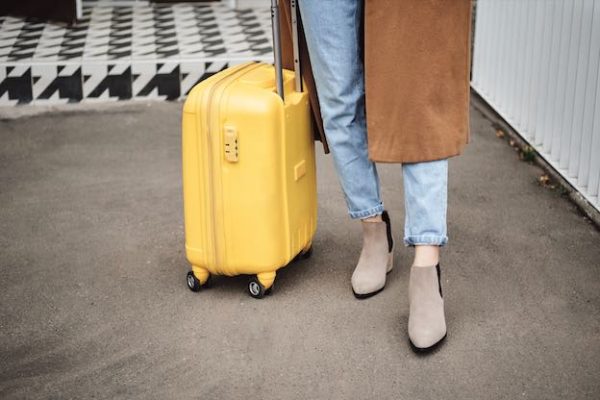 Close up stylish girl in coat standing with yellow suitcase on street